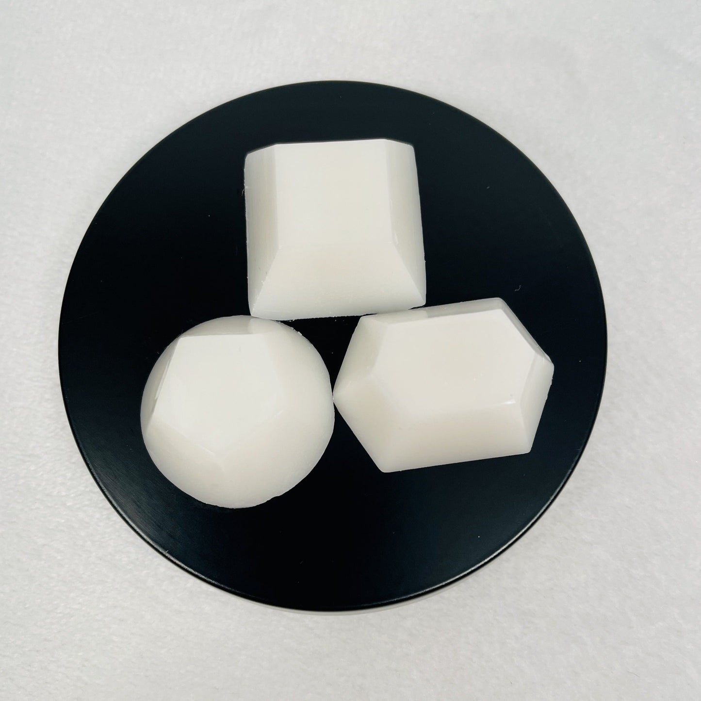 Three different wax melt shapes sitting on top of a black tin lid.